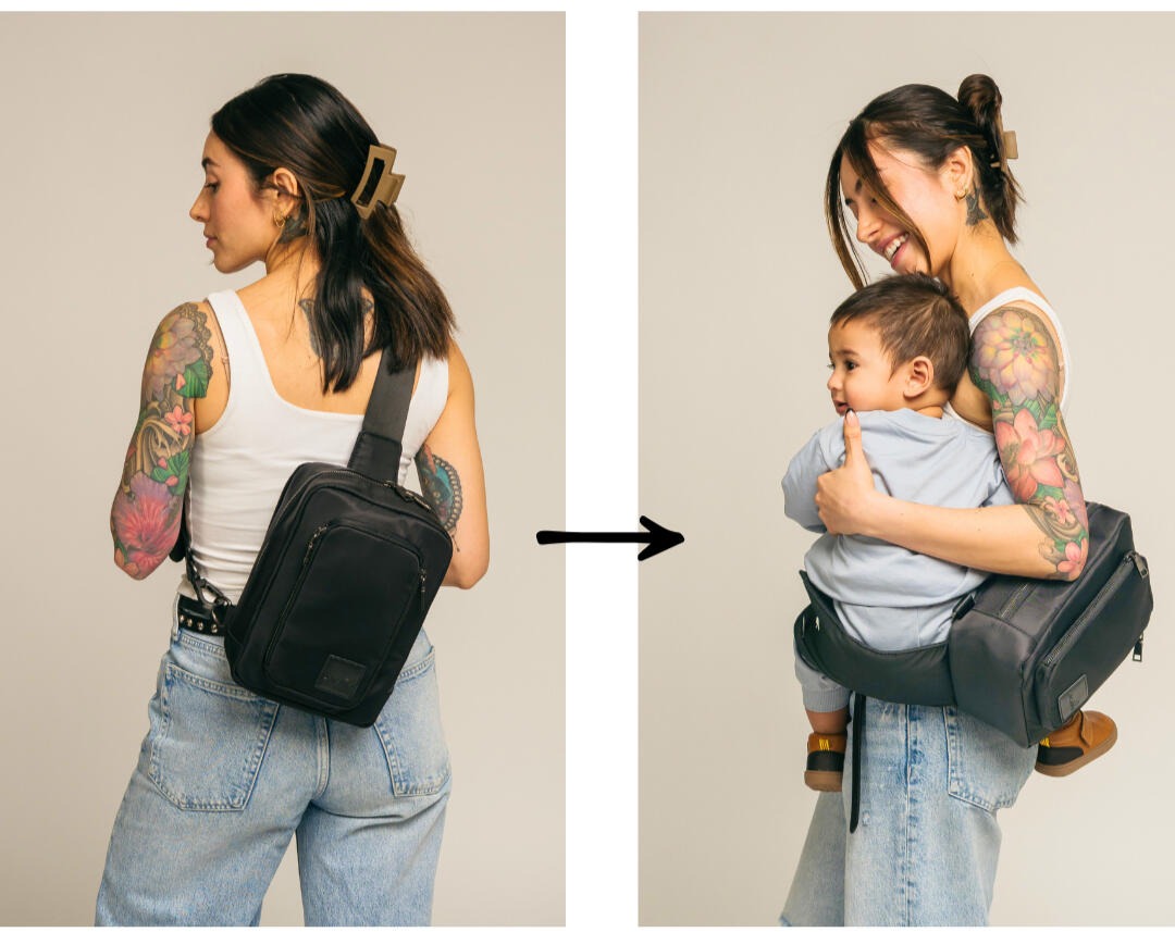 Mom carrying a toddler in a sleek black Jacana convertible baby carrier and diaper bag while walking through a city park.