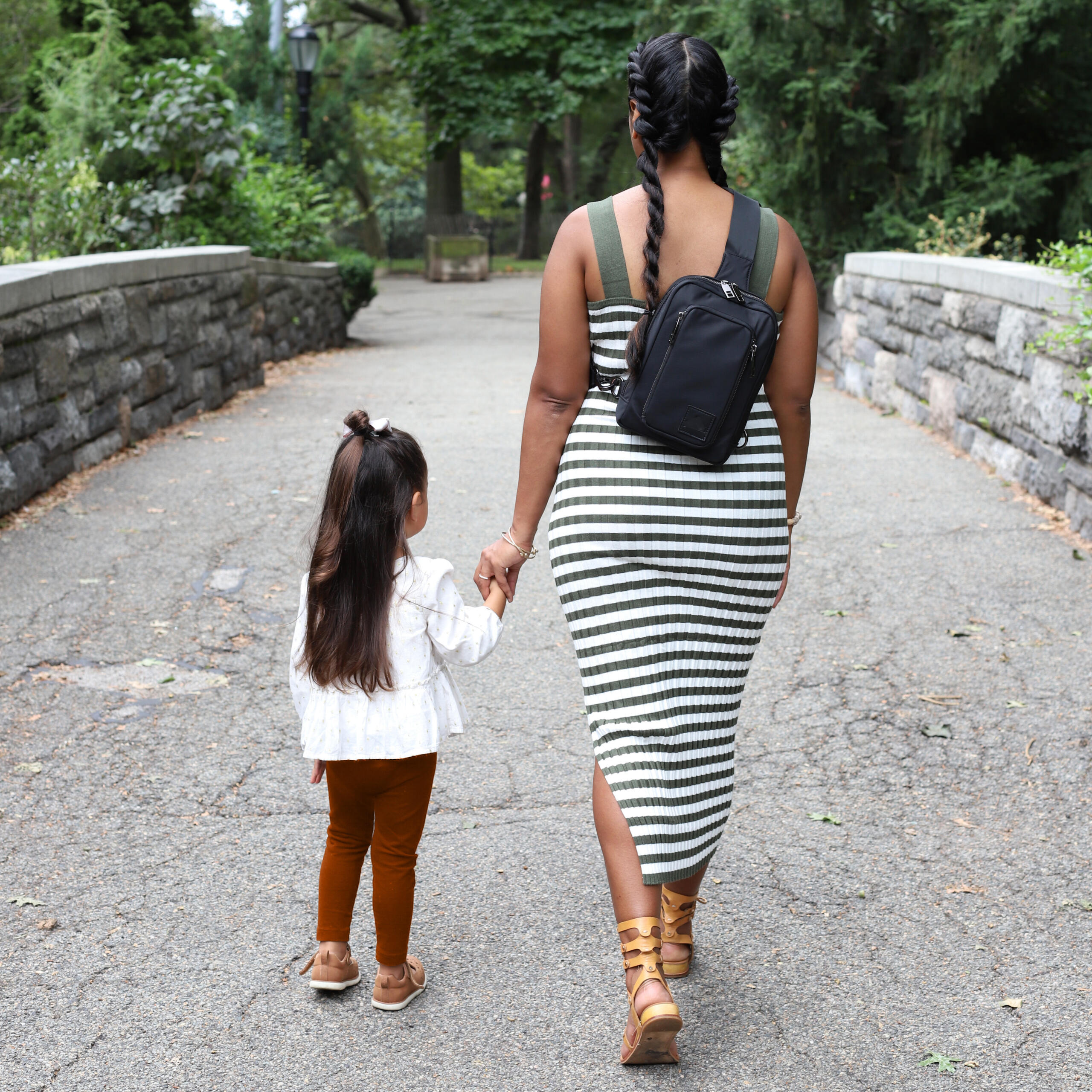 Mom wearing the sleek black patent-pending convertible baby carrier and diaper bag while walking through the park.